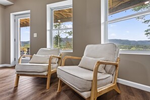 Two wooden chairs with cushions in a room with large windows and a view of the outdoors.