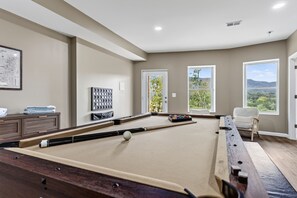 A pool table in a room with large windows, a map on the wall, and a door leading outside.