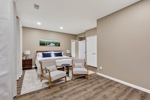 A bedroom with a bed, two chairs, a nightstand, a lamp, and a painting on the wall.