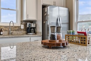 Une cuisine dotée de plans de travail en granit, d’une machine à café, de salières et de poivrières, et d’un réfrigérateur.