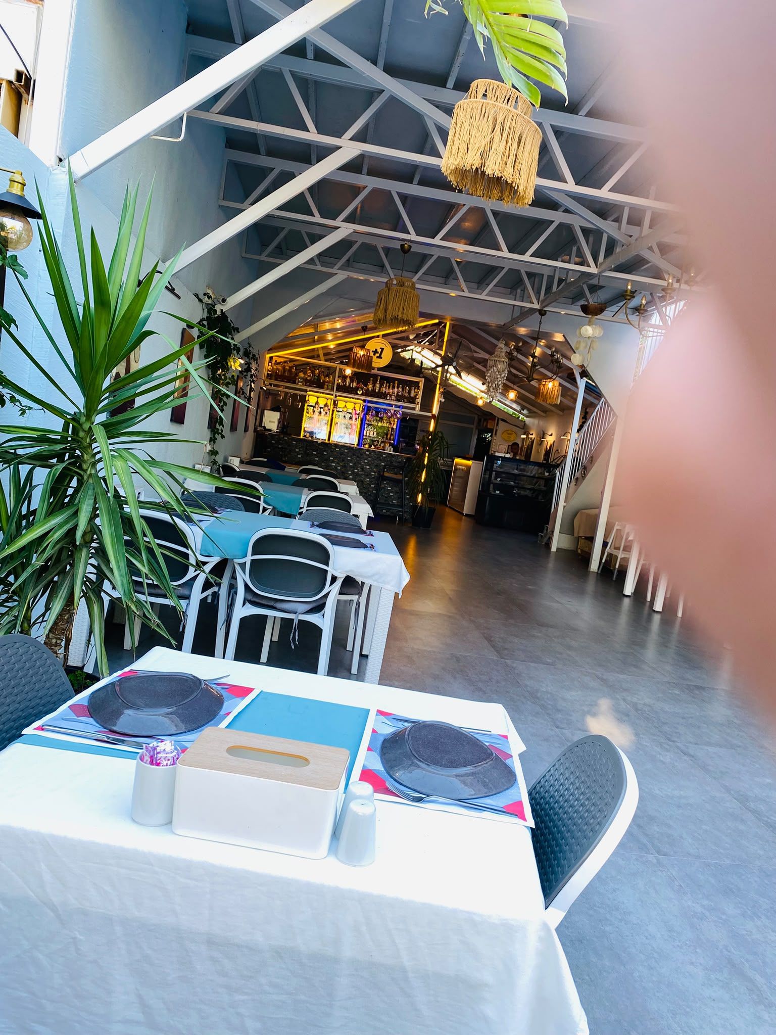 Een eetruimte met tafels voor twee personen, stoelen en een bar op de achtergrond.