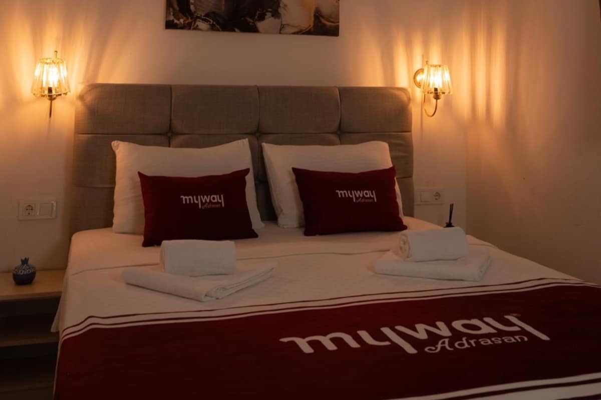 Una habitación de hotel con una cama, dos lámparas adosadas a la pared y un cuadro sobre la cama.