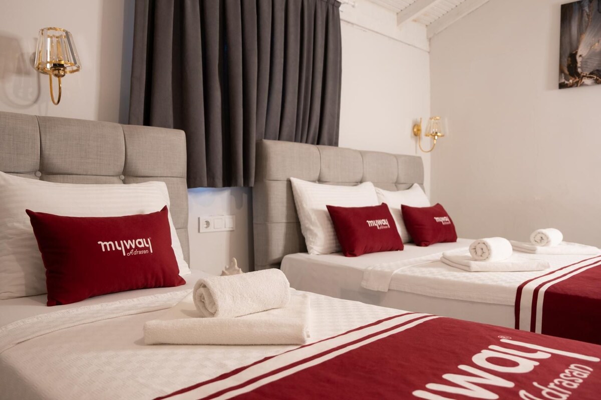 Habitación de hotel con dos camas, cada una con almohada roja y manta blanca. Hay dos apliques de pared y un cuadro en la pared.