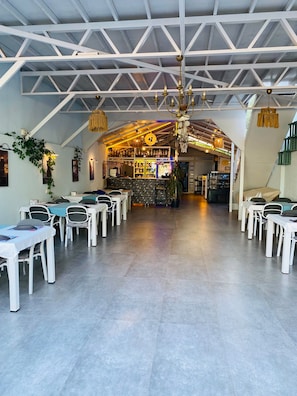 Un restaurante con una zona de bar, mesas y sillas blancas.