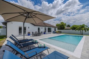 Un giardino con piscina, sedie a sdraio e una veranda coperta.