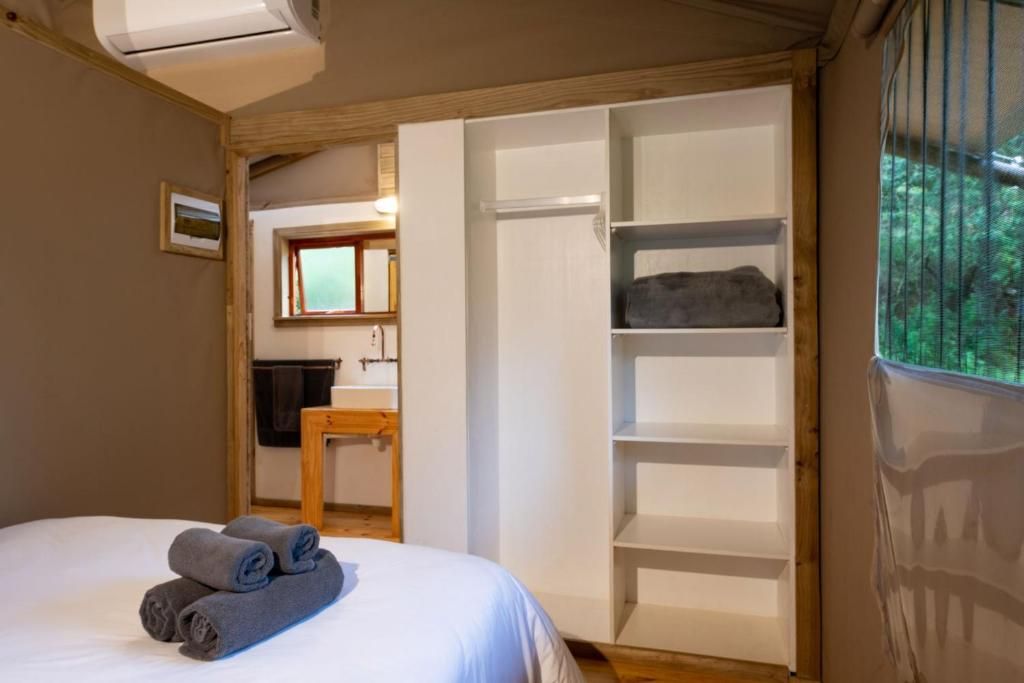 A bedroom with a bed, a wooden nightstand, a window with blinds, and a built-in wardrobe.