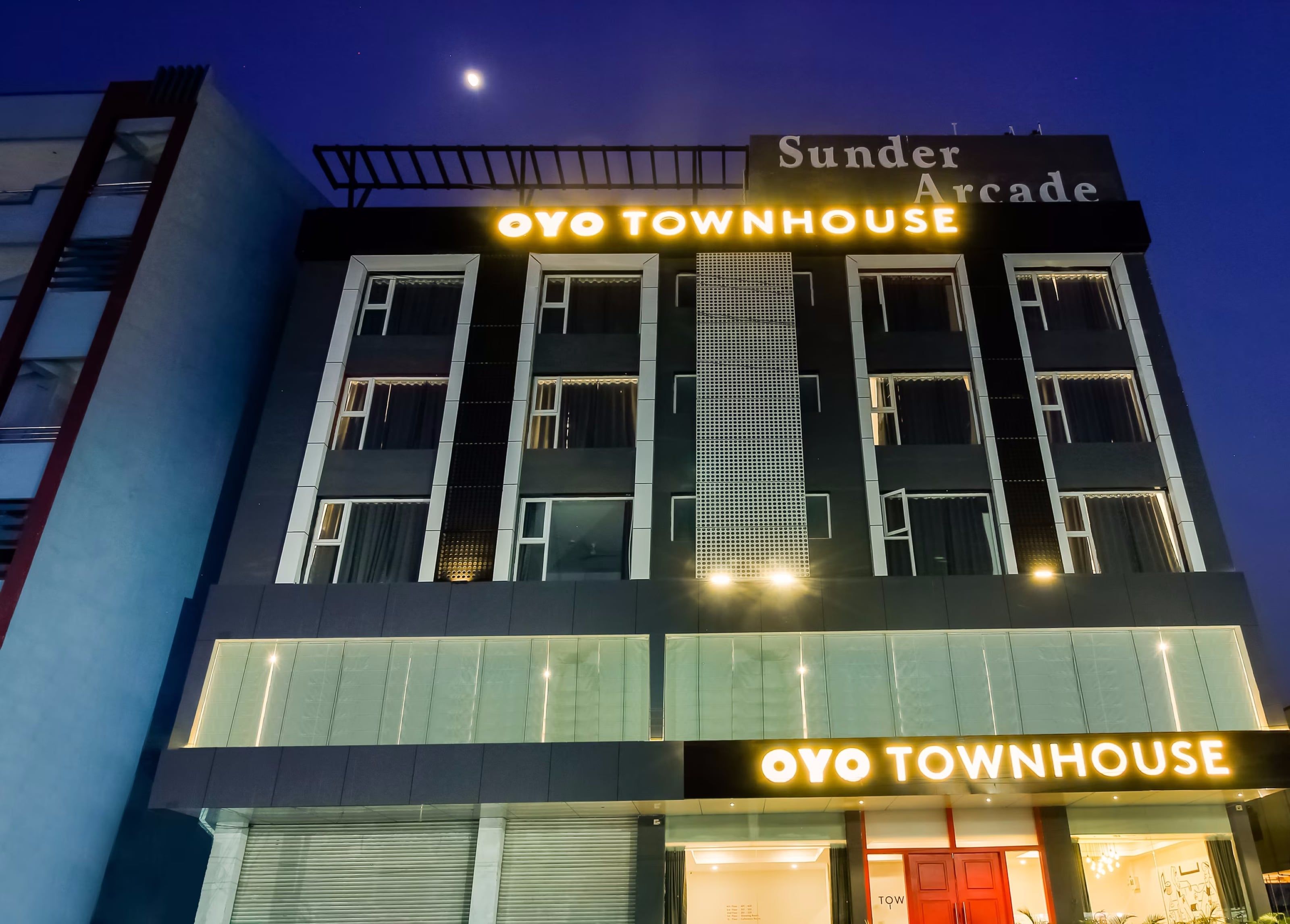 A building with a sign reading 'Sunder Arcade' and 'Oyo Townhouse' with a modern architectural design, featuring multiple windows and a visible balcony.