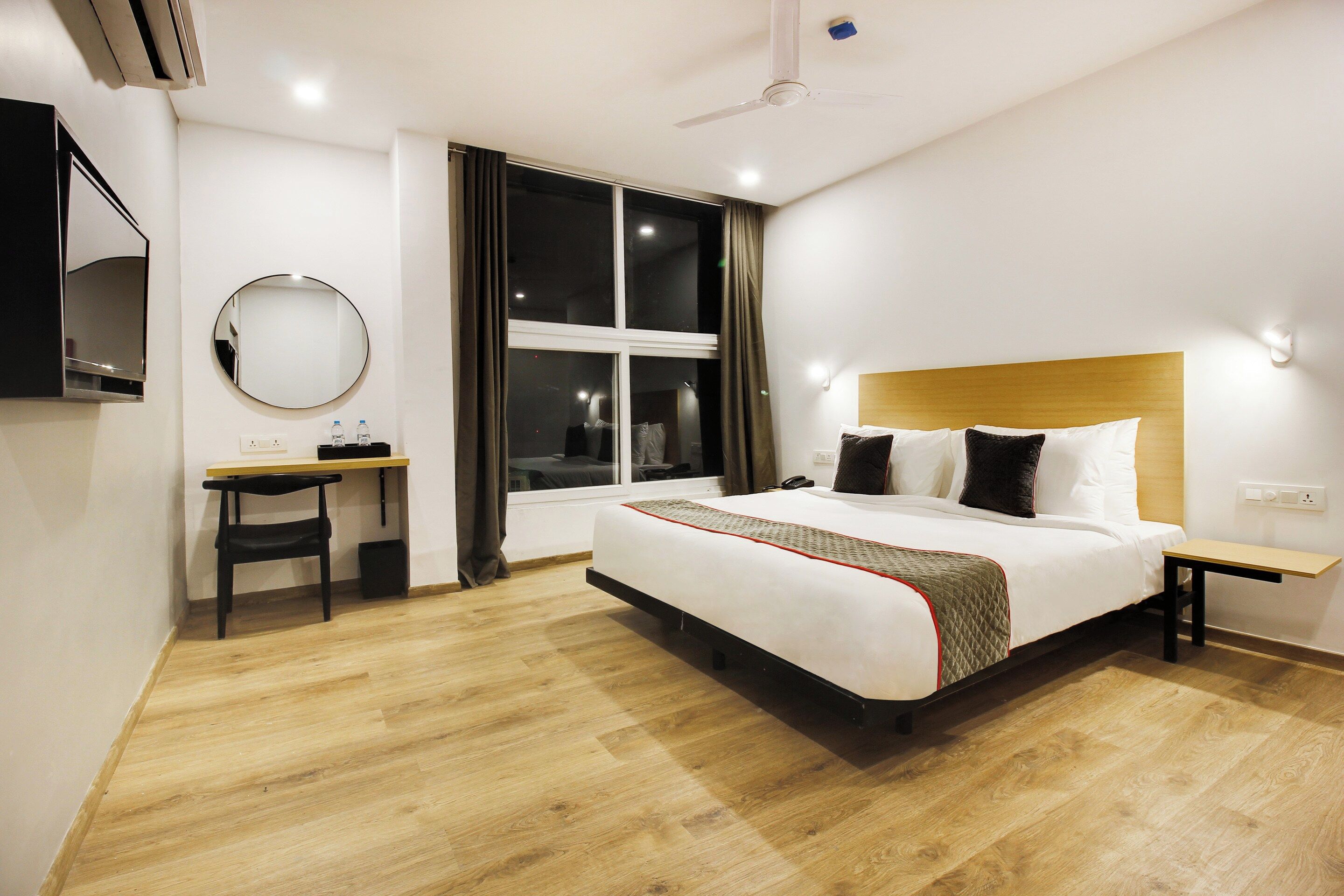 A hotel room with a bed, bedside table, desk, chair, and a window with curtains.
