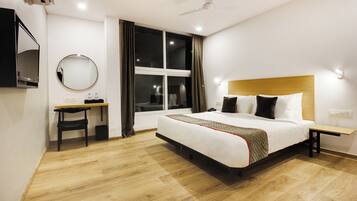 A hotel room with a bed, bedside table, desk, chair, and a window with curtains.