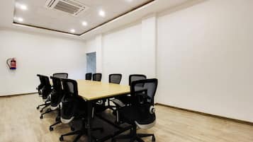 A conference room with a long table and six chairs, a fire extinguisher on the wall, and a door in the background.
