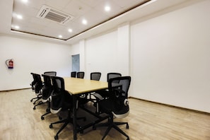 Un salón de conferencias con una larga mesa y seis sillas, un extintor en la pared, y una puerta al fondo.