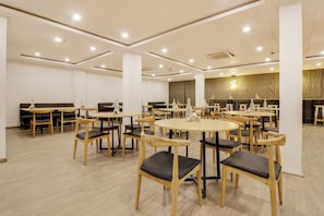 A spacious dining area with multiple round tables and chairs, a high ceiling with recessed lighting, and a neutral color palette. - Super townhouse moosapet Rcc Prime (Hyderabad)