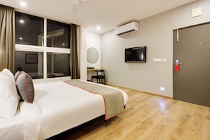 Quarto de hotel com cama, escrivaninha, cadeira, televisão e ar condicionado.