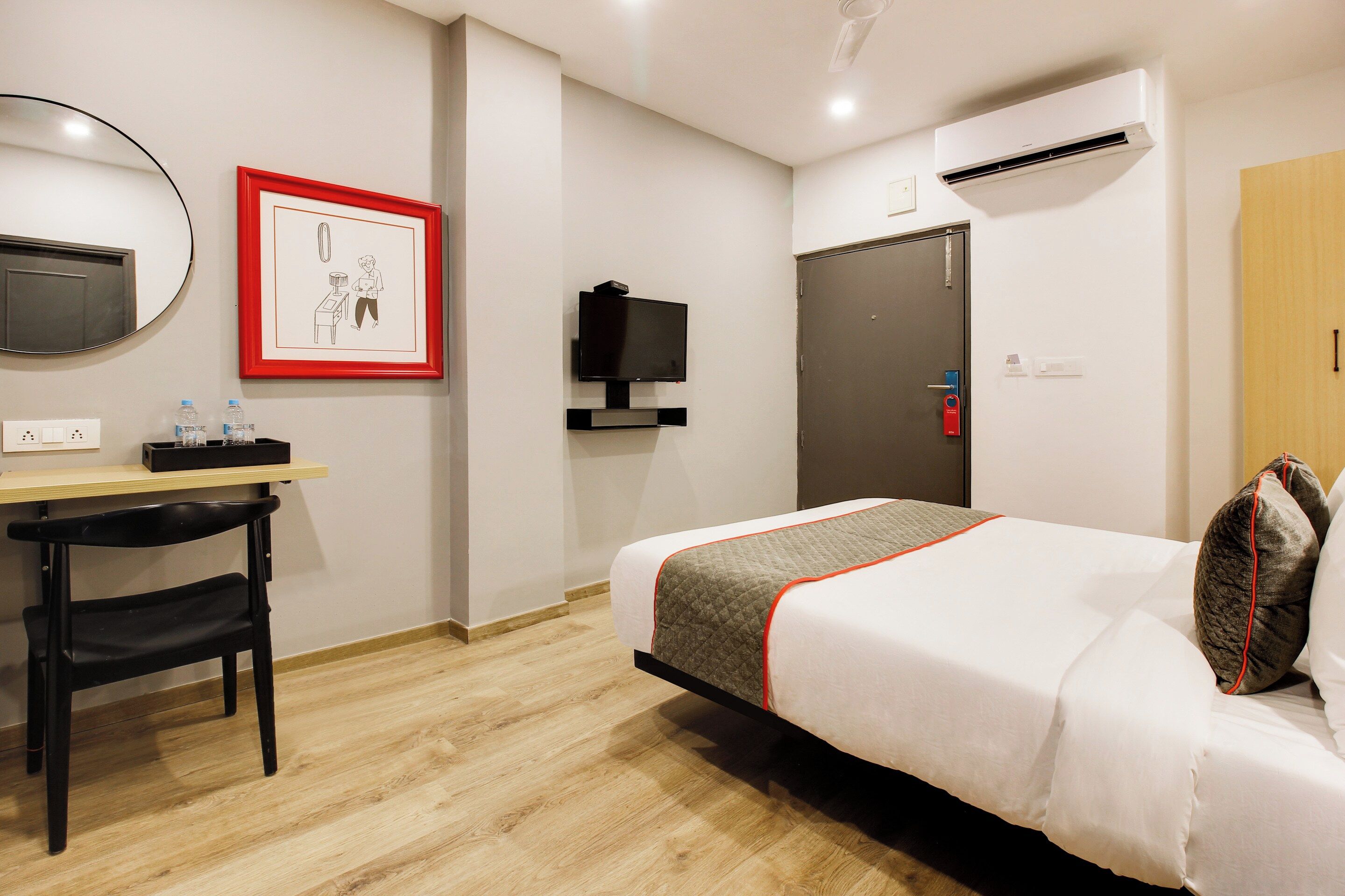 A hotel room with a bed, desk, chair, TV, and a door with a lock.