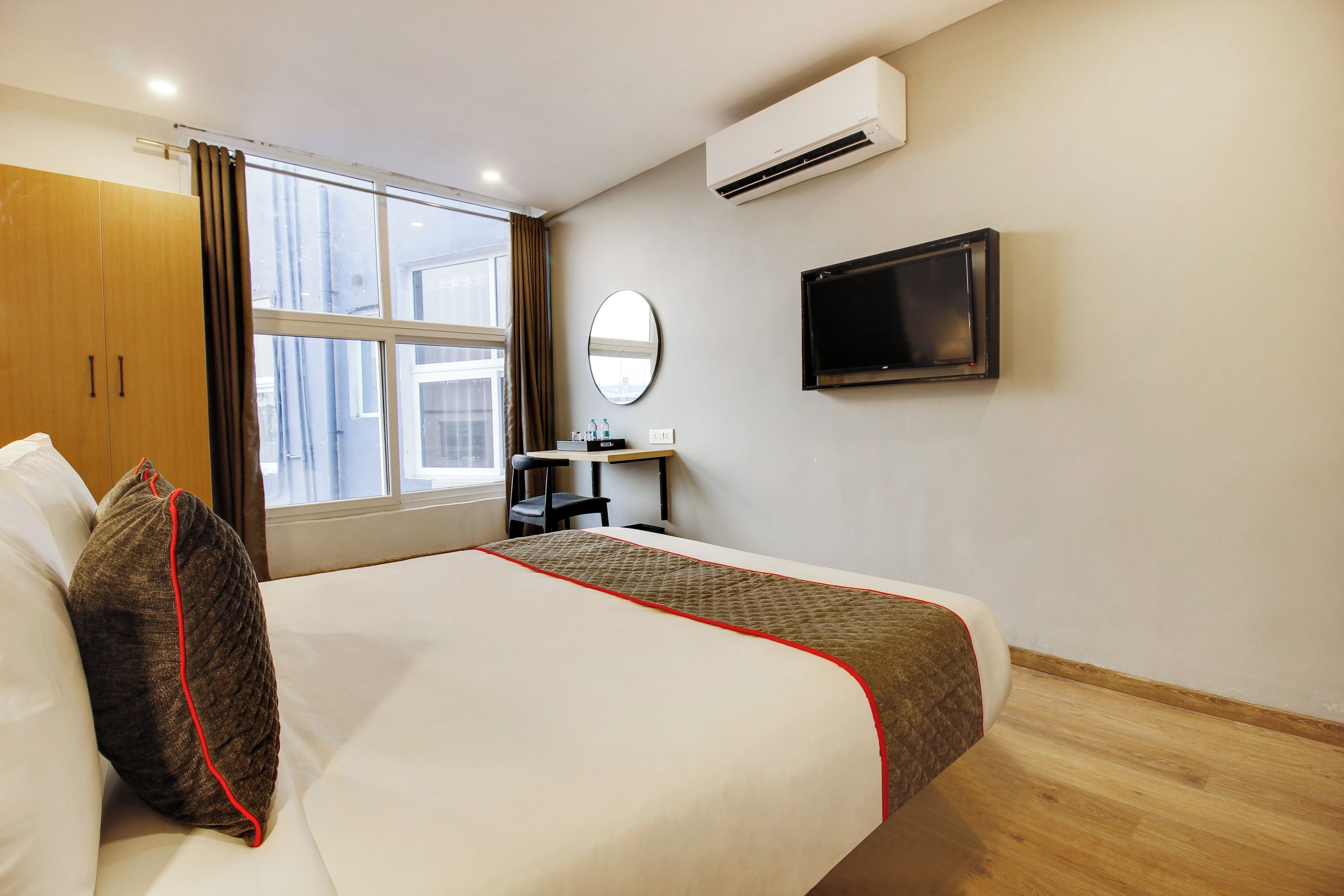 A hotel room with a bed, a desk, a chair, an air conditioning unit, a TV, and a window with curtains.