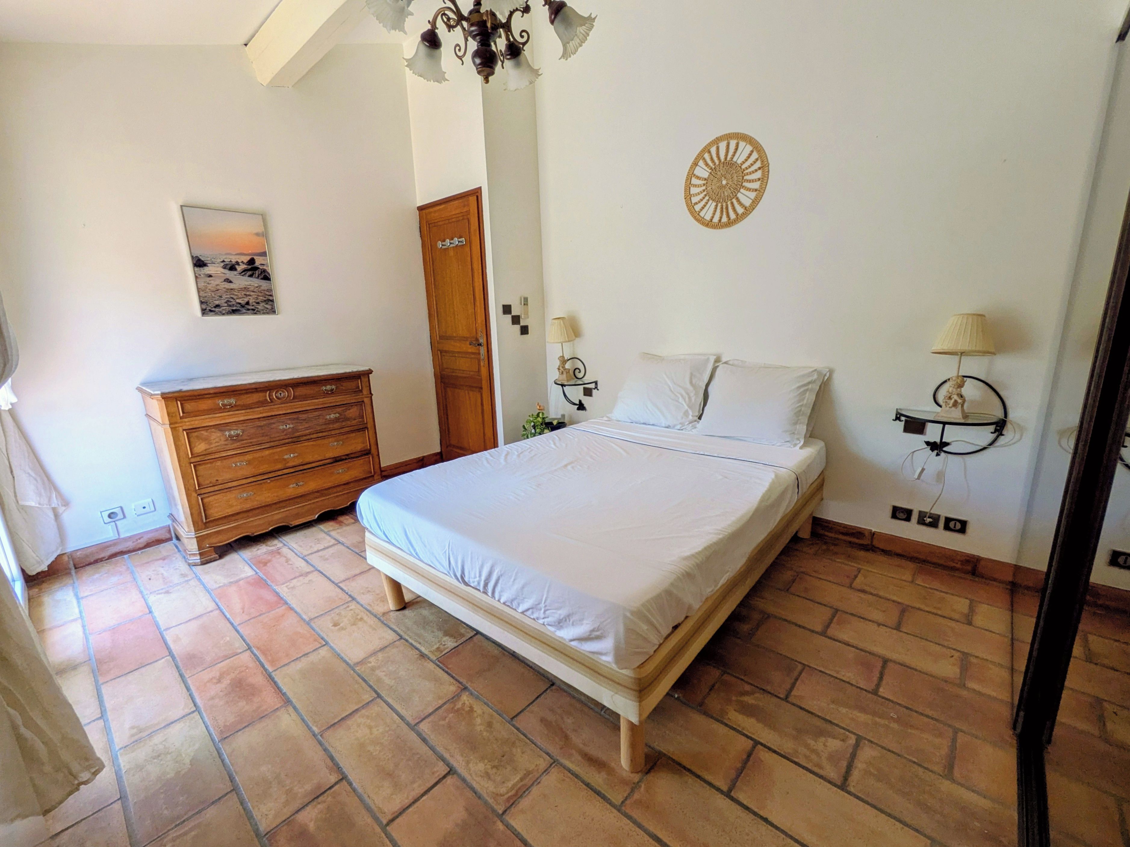 Une chambre à coucher avec un lit, une commode et une lampe fixée au mur.