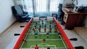 Une pièce avec une table de baby-foot, un bureau avec un ordinateur et une fenêtre avec des rideaux.