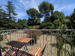 A wooden deck with metal railings, overlooking a garden with various trees and shrubs. - Alexandre's Farmhouse (Arles)
