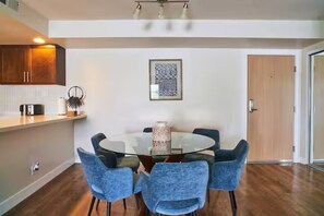 Un coin repas avec une table ronde en verre et six chaises, un espace cuisine doté de meubles en bois et une décoration murale à motifs.