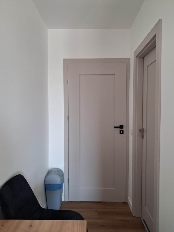 Un couloir avec une porte fermée, une poubelle et une chaise.