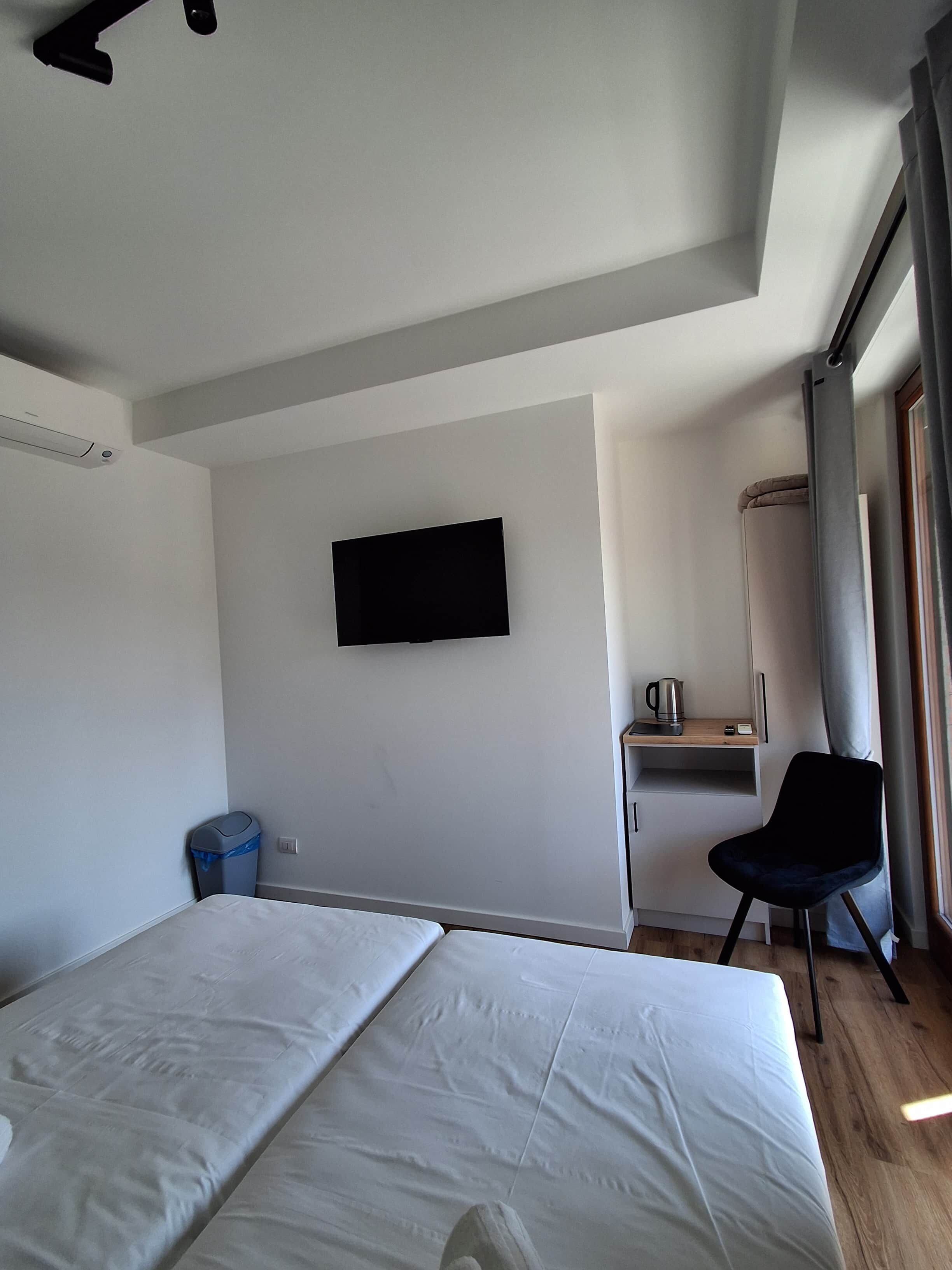 Une chambre d’hôtel avec un lit, un bureau, une chaise, une télévision et une fenêtre avec des rideaux.