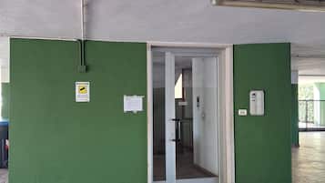 A hallway with green walls, a tiled floor, and a door leading to another room. There are signs on the walls and a vent on the ceiling.