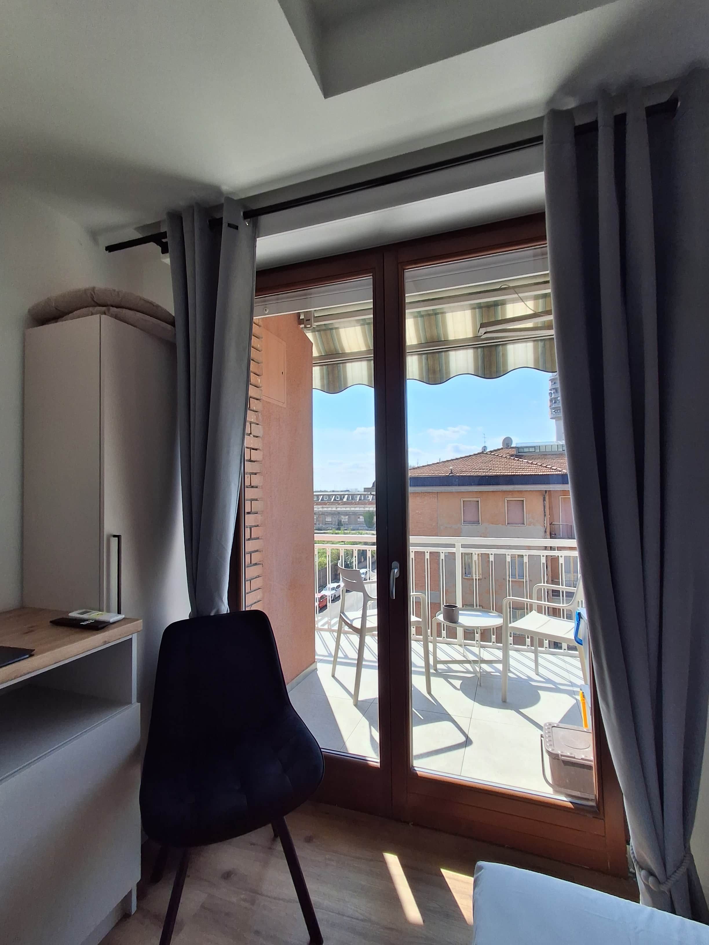 Une pièce dotée d’une porte-fenêtre coulissante donnant sur un balcon aménagé avec du mobilier d’extérieur.