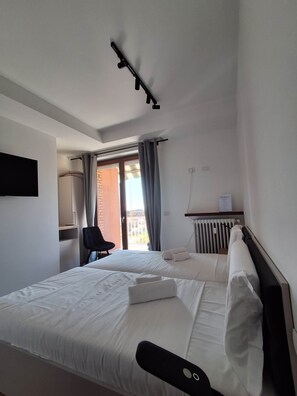 A hotel room with a bed, a chair, a desk, a radiator, and a window with curtains. - defaultName (Verona)