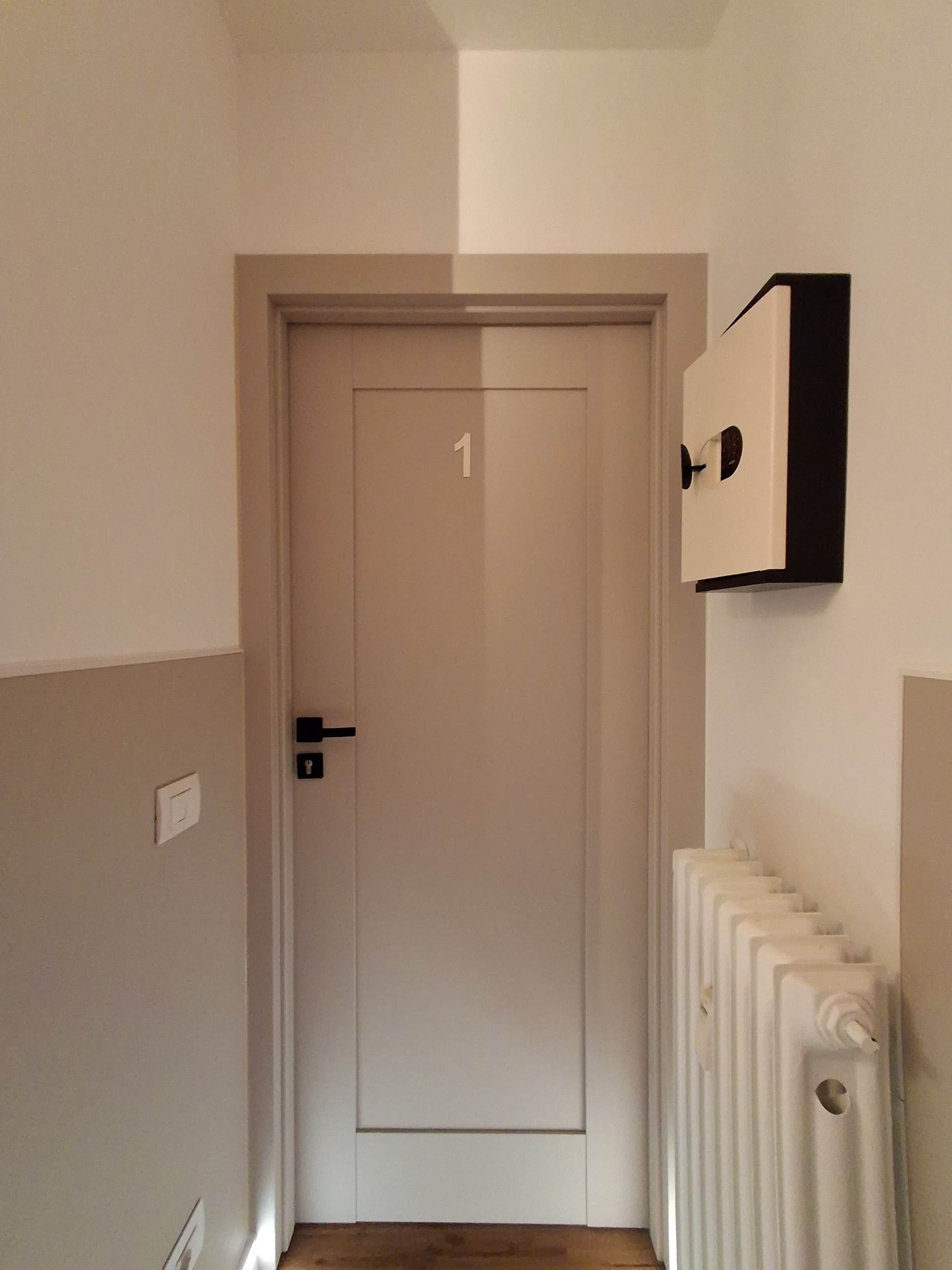 Un couloir avec une porte portant le numéro 1, un radiateur sur le côté droit et un interrupteur sur le mur.