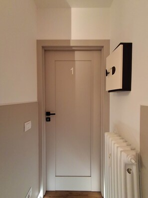 Un couloir avec une porte portant le numéro 1, un radiateur sur le côté droit et un interrupteur sur le mur.