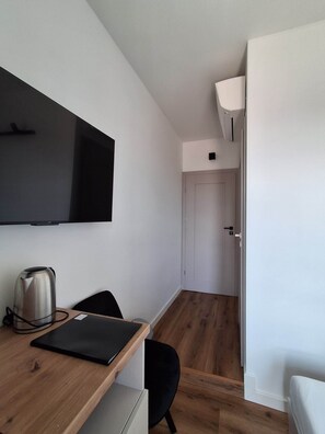 Ein modernes, kompaktes Zimmer mit einem Holztisch, einem schwarzen Stuhl, einem flachbildfernseher an der Wand, einem Wasserkocher und einer Tür zu einem weiteren Raum.