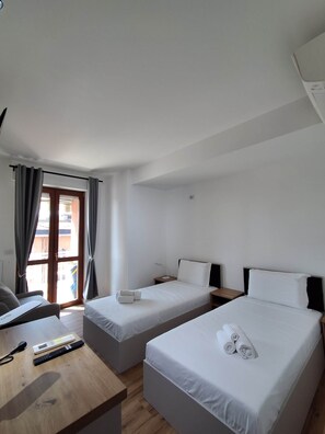 Ein Hotelzimmer mit zwei Einzelbetten, einem Schreibtisch mit Computer und Fernbedienungen, einem Fenster mit Vorhängen und Blick ins Freie.