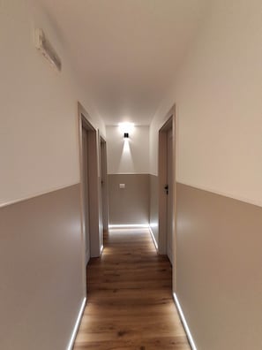 Ein schmaler Flur mit Holzboden, weißen Wänden und einer Deckenleuchte.