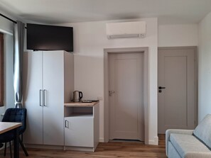 A compact room with a kitchenette, a flat-screen TV mounted on the wall, a door, and a sofa. - Porta Fiera | Room 4 (Verona)