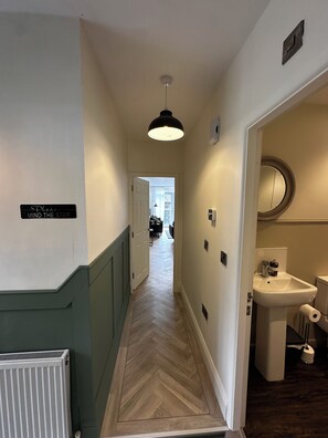 Ein Flur mit einem Schild an der Wand, einem Heizkörper, einer Leuchte und einem Badezimmer mit Waschbecken und Toilette.
