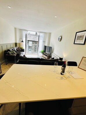 A modern living room with a sofa, a TV, and a dining table with wine glasses. - Spacious Luxury 3 bedroom cottage with stylish interior and en-suite bathrooms (Bowness-on-Windermere)