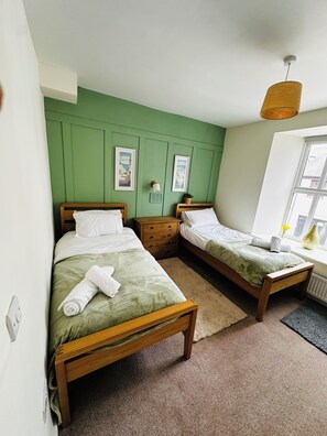 A room with two wooden beds, a green wall, a window with a view, and a hanging light fixture. - Spacious Luxury 3 bedroom cottage with stylish interior and en-suite bathrooms (Bowness-on-Windermere)