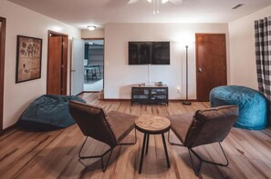 A living room with a sofa, two bean bags, a coffee table, a TV, and a floor lamp. - Bigfoot's Hideout - Cabin-Game Room Sleeps 10 (Logan)
