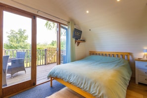 A bedroom with a bed, a nightstand, a TV, and a sliding glass door leading to a balcony. - Charming Stay In A Mid Wales River Escape (Llangammarch Wells)
