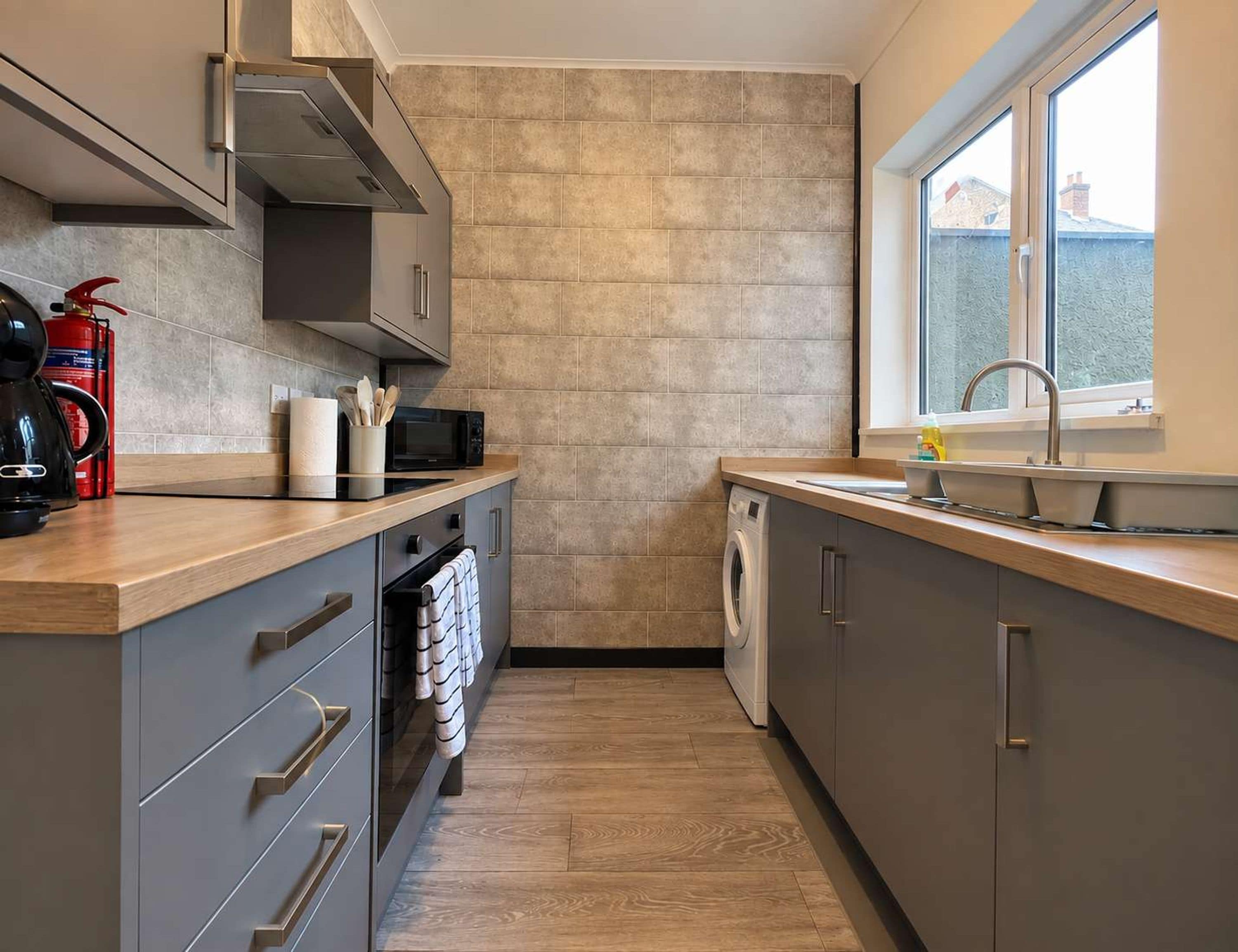 Een moderne keuken met grijze kastjes, een magnetron, een waterkoker en een wasmachine.