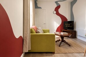 Ein Wohnzimmer mit einem grünen Sofa, einem Holztisch und einem Fernseher auf einem Schrank.