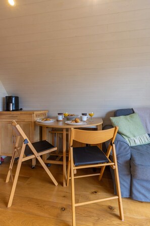 A compact living space with a wooden dining table, two chairs, a sofa, and a kitchenette area. - Riverside Glamping Pod With Free Wifi Parking (Llangammarch Wells)