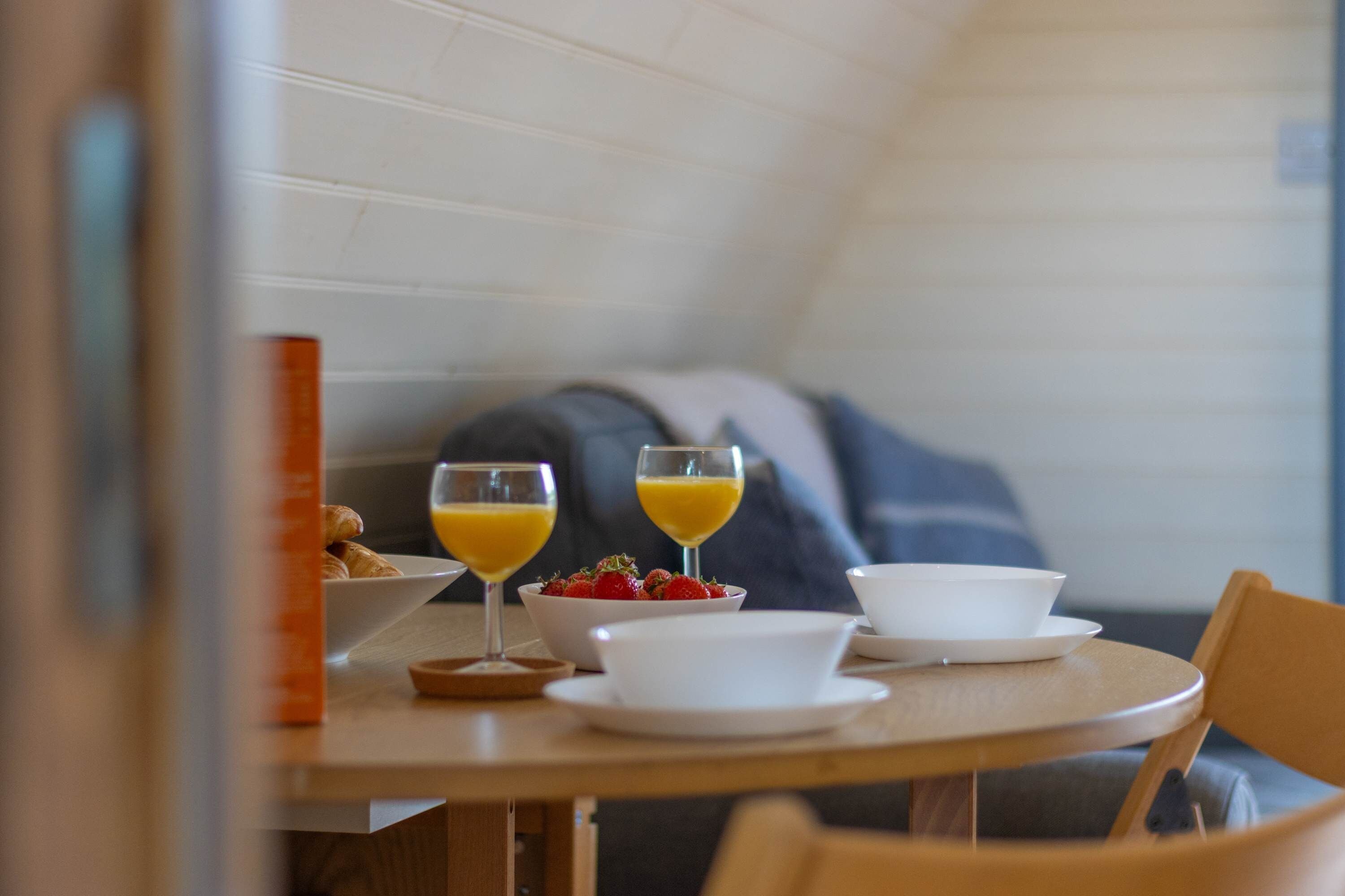 A breakfast setting with croissants, a bowl of strawberries, and two glasses of orange juice on a wooden table.