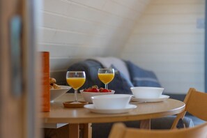 A breakfast setting with croissants, a bowl of strawberries, and two glasses of orange juice on a wooden table. - Riverside Glamping Pod With Free Wifi Parking (Llangammarch Wells)