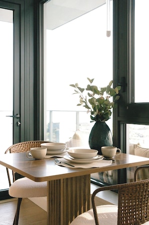 A dining table with plates, cups, and a vase of greenery, set in a room with a view through a glass door. - The Silhouette Nest | 2BR+2BA | Pool&Sauna (Kelowna)