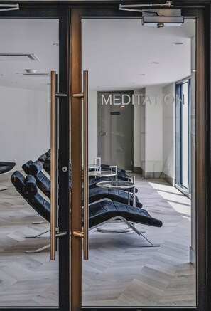 A modern room with a glass door, a meditation area with chairs, and a herringbone-patterned floor. - The Silhouette Nest | 2BR+2BA | Pool&Sauna (Kelowna)