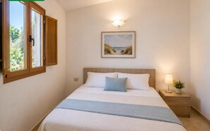 A bedroom with a bed, a nightstand, a lamp, a window with curtains, and a painting on the wall. - Apartment With Shared Pool a Stone's Throw From the sea (Nicotera)