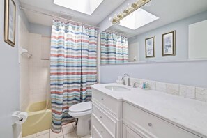 Une salle de bain avec un rideau de douche, des toilettes, un lavabo et un miroir.