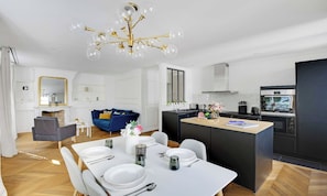 Een moderne keuken met een centraal eiland, een eethoek met een wit gedekte tafel, en een zithoek met een blauwe bank.