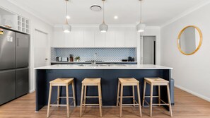 A modern kitchen with a central island, bar stools, a refrigerator, and a patterned backsplash. - Culburra Cove - Pet Friendly - 5 Mins Walk to the Beach (Culburra Beach)